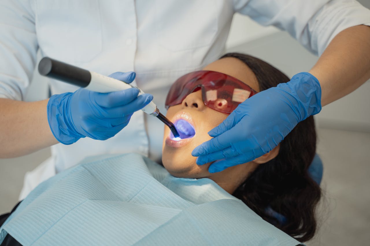 Dentist performing dental treatment using curing light on patient wearing protective eyewear.