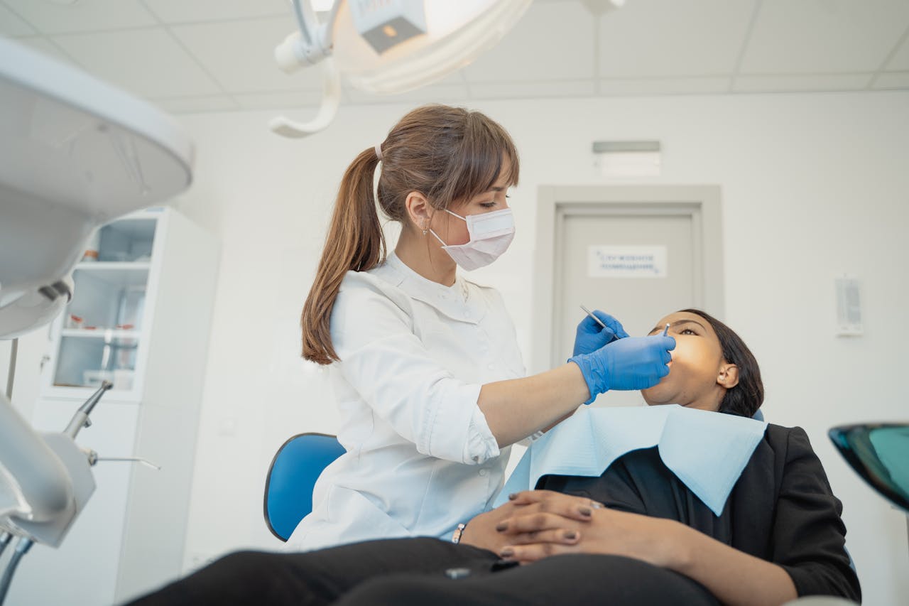 A female dentist wearing a facemask examines a patient in a modern dental clinic setting.